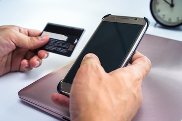 Online payment Concept. Man using credit card and Office desk table with computer, clock