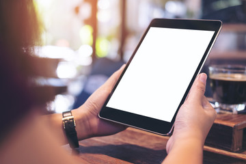 Mockup image of hands holding black tablet pc with blank white screen with white coffee cup and tea on wooden table in cafe