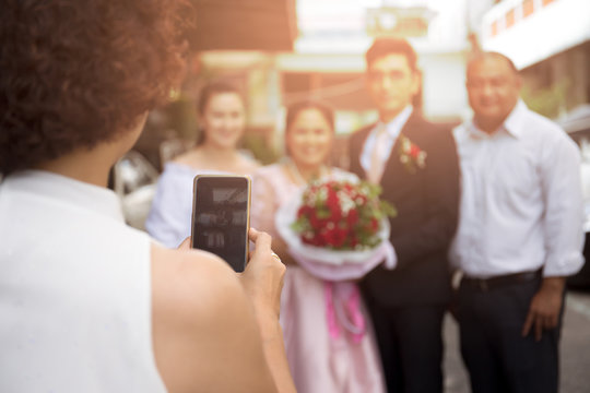 Woman taking picture of groom and bride with guest on cell phone