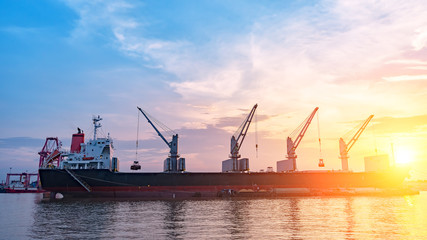 Background for cranes and industrial cargo ships in port at twilight.