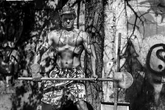 Photo outdoor of a man with a good torso with a shovel and a cowboy hat