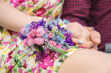 Young newlyweds are holding hands with a bouquet that lies on the bride's lap