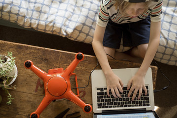 Overhead view of boy working on laptop by drone at home