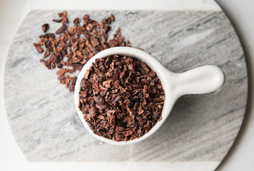 Chocolate nibs in white cup on white & gray marble