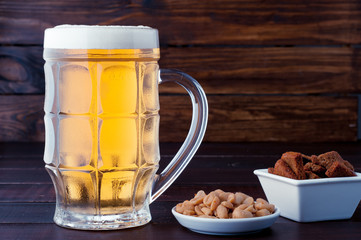 glass of cold frothy lager beer and plate of snacks on wooden table