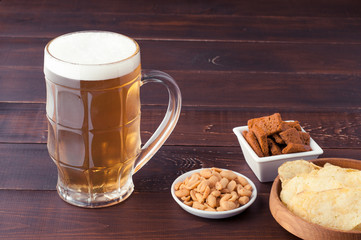 glass of cold frothy lager beer and peanuts plate on wooden table
