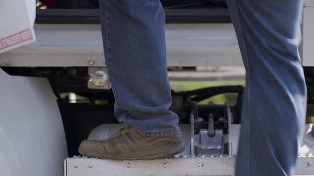 Detail of driver's feet climbing down from truck cab in daylight exterior, summer day. Side view, slow motion 4K recorded at 60fps.
