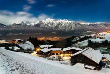 Snowy landscape with traditional village at the Austrian Alps under the moonlight in winter
