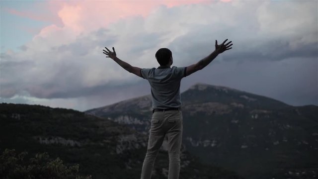 Man on top of mountain raising hands up succes slow motion shallow dof. Strong male silhouette holds hands up expressing inspiration reward determination achievement concept in Alps destination Europe