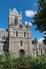 Fototapeta na wymiar Dublin, Ireland - August 7, 2017: Gray stone bell tower and chancel of Christ Church Cathedral against blue sky with white clouds. Green vegetation.
