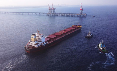 Large bulk carrier ship pulled by tugboats in open water