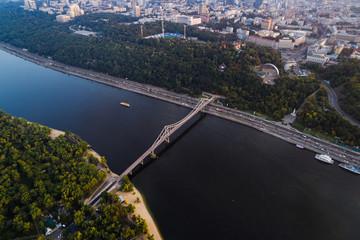 Obraz premium Panoramic view of the city center of Kiev. Aerial view of the right bank of Kiev with the Dnieper River, a pedestrian bridge and a large park area at sunset.