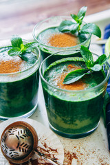Crop shot of green smoothies with leaves of fresh mint on the kitchen desk