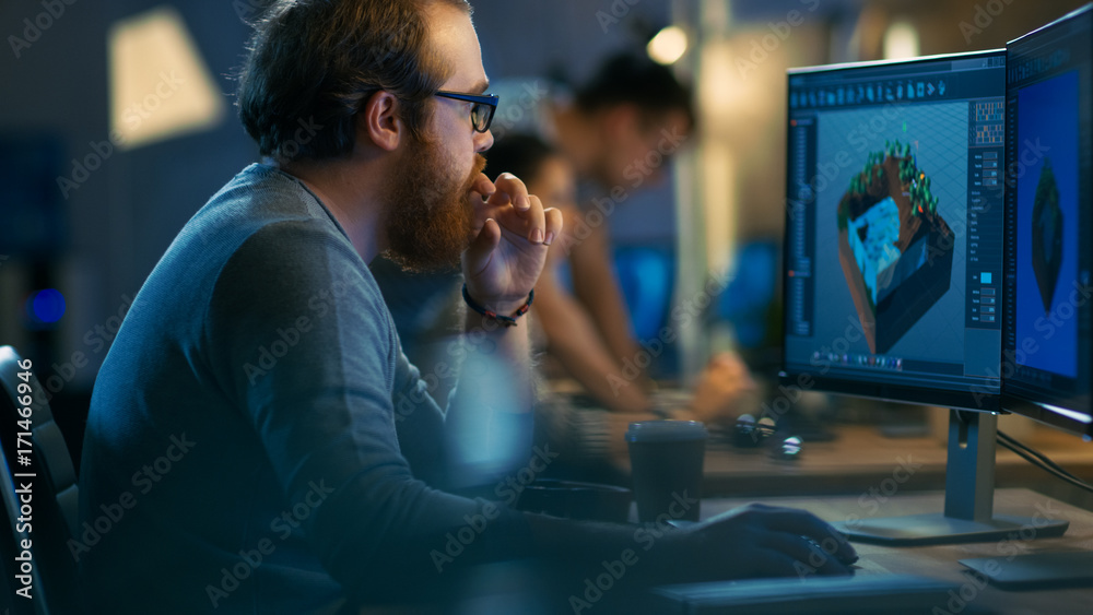 Poster Male Game Developer works on a Level Design on His Personal Computer with Two Displays. He Works for in a Creative Office Environment with Very Talented Colleagues.