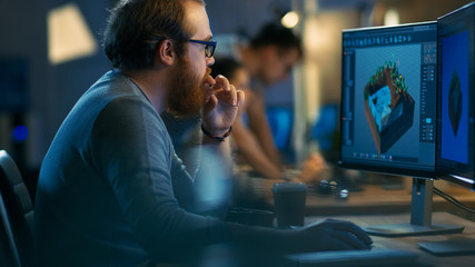 Male Game Developer works on a Level Design on His Personal Computer with Two Displays. He Works for in a Creative Office Environment with Very Talented Colleagues.