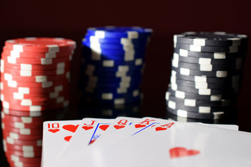 Poker hand royal flush on black reflective board. Poker chips on background.