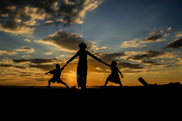Silhouette of mother and kids.Happy family in mother's day concept,I Love you mom.Asian mother and little cute daughter playing together.Mother,daughter and son greeting and hug together with sunset