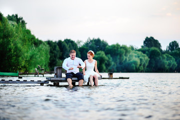 Beautiful young wedding couple, bride and groom posing on lake background. The groom and the bride on pier