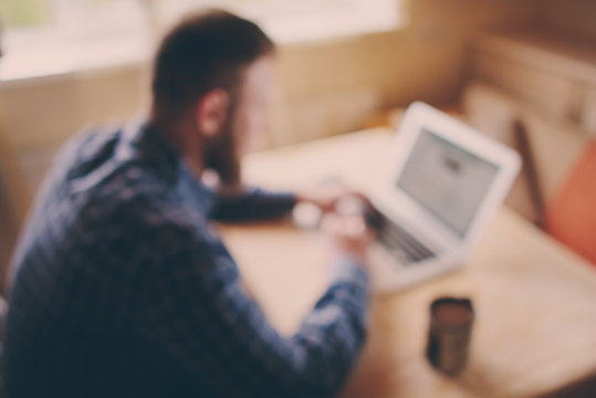 Blurred Background, Businessman Using Laptop At Workplace - Rear View