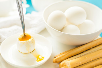 Fototapeta na wymiar Traditional breakfast: soft-boiled eggs, green tea and bread sticks on white wooden desk. Selective focus