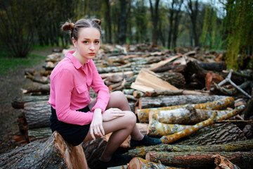 Beautiful young woman sitting on stack of felled tree trunks in the forest