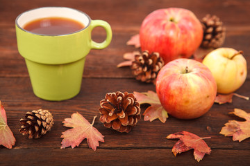 Autumn concept, fallen red-yellow leaves with apples, pine cones and a cup of tea on a wooden table. Thanksgiving Day.
