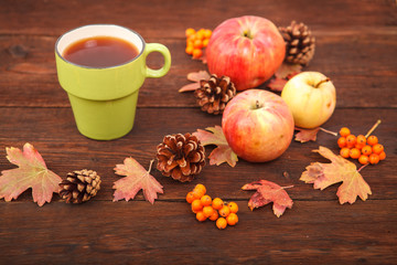 Autumn concept, fallen red-yellow leaves with apples, pine cones, rowan and a cup of tea on a wooden table. Thanksgiving Day.