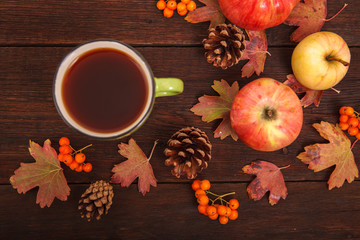 Autumn concept, fallen red-yellow leaves with apples, pine cones and a cup of tea on a wooden table. Thanksgiving Day.