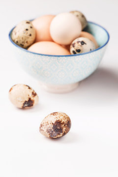 Chicken and quail eggs in blue bowl, white background, vertical, selective focus