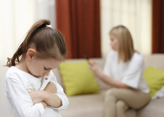 Sadness young girl. Portrait of bored daughter with mother using cellphone on bed.