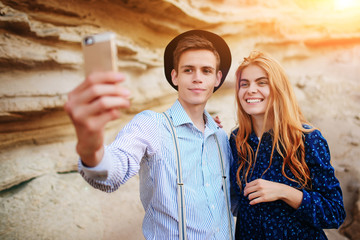 Attractive man with a beautiful woman are hugging and smiling. They are making selfie on the background of sand quarry