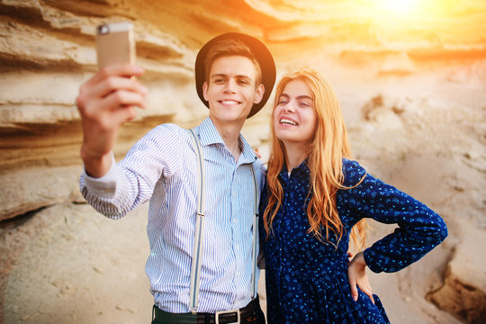 Attractive man with a beautiful woman are hugging and smiling. They are making selfie on the background of sand quarry