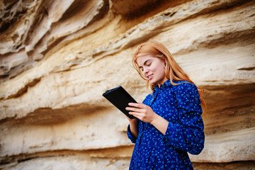 Beautiful woman smiling and looking at the screen of a tablet on the background of a sand quarry