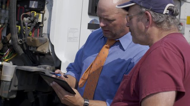 Insurance agent, or other official with electronic notepad, talks to truck driver and makes notes during an inspection of truck engine. Close up view from front angle. Hand-held 4K