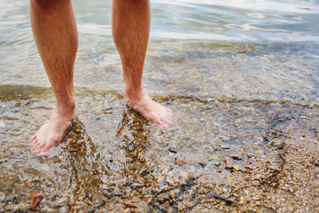 Close up background of man's feet standing in a clear water with pebble bottom
