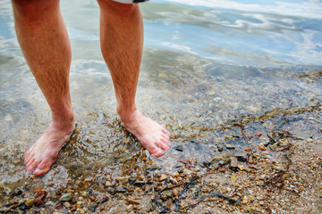 Close up background of man's feet standing in a clear water with pebble bottom