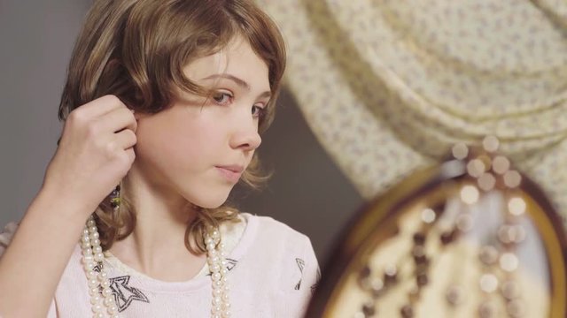 Little girl looking at mirror reflection, fitting mother's earring, childhood