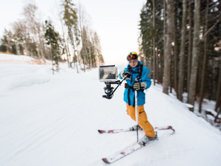 Fototapeta na wymiar Skier man taking selfie with stick over forest on the winter resort. Focus on his camera, blurred background