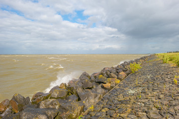 Dike along the shore of a stormy lake in sunlight in summer
