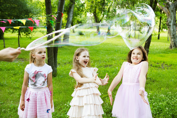 Children playing with bubbles children's holiday in Park. Group of kids celebrate birthday party together in the summer outdoors.
