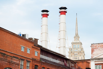 Mix of two pipes and buildings of different times against blue sky. Old Industrial building of the...