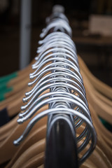 Closeup of clothes on hangers on a rack for a store, emphasizing the metal parts of the hangers that pass through the picture in a symmetrical line giving an abstract feeling to the whole.