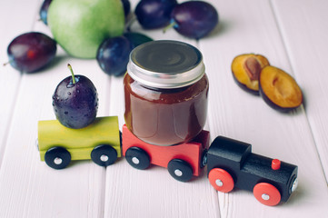 Jar with baby food plum puree and fresh plum on the toy wooden train