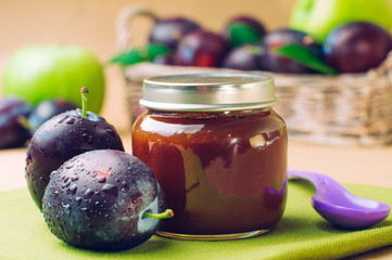 Jar with baby food plum puree with spoon near fresh plums