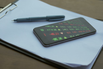 close-up phone with shares on the stock exchange lies on a clipboard with a paper next to lies a pen