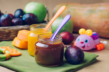 Jars with baby food plum and pumpkin puree with spoons near fresh fruits