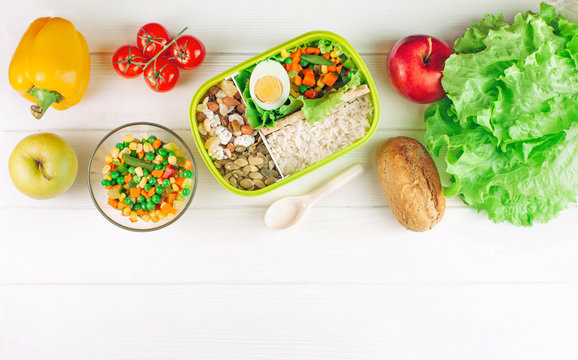 Lunch box filled with rice and mixed vegetables on white wooden background
