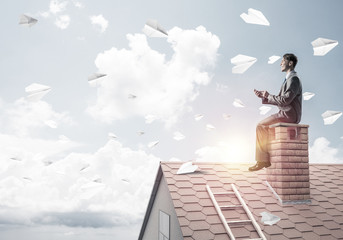 Man on brick roof reading book and paper planes flying in air