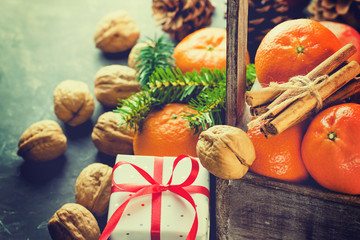 Christmas Gift Box with Red Silk Ribbon Tangerines Cinnamon Sticks Fir Tree Branches Pine Cones Walnuts in Wood Box Black Background Greeting Card Poster Copy Space