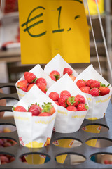 A rack of white bags full of red strawberries in a market stall with in the background a yellow...